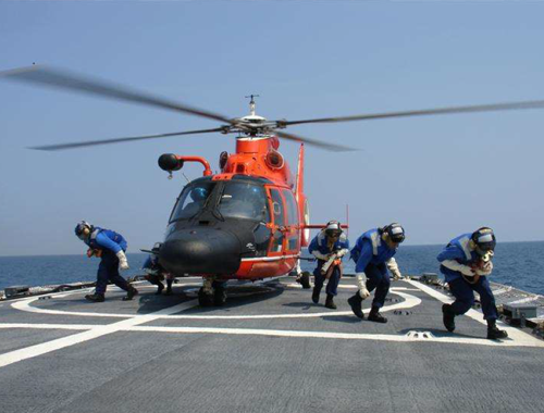 Crewmembers conduct flight deck operations with a MH-65 helicopter.